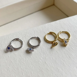 Macro detail of silver and gold Evil Eye earrings with blue gemstones and white diamonds