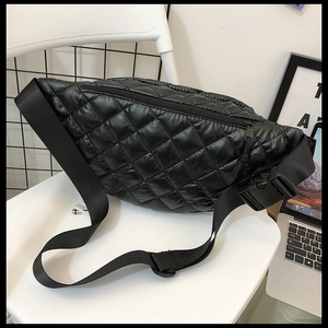 Close-up of black quilted nylon waist bag with adjustable strap on a white chair