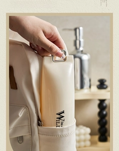 Cream portable travel toiletry case with metal handle being placed into a backpack