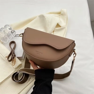 Brown leather saddle bag with wide woven strap and gold hardware in lifestyle setting