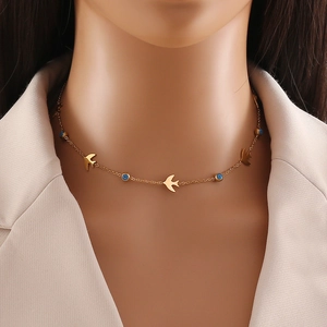 Detail of gold layered necklace with bird and blue eye pendants on model wearing a blazer