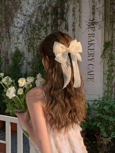 Creamy mesh bow hair clip with long ribbons worn by a model in a garden setting