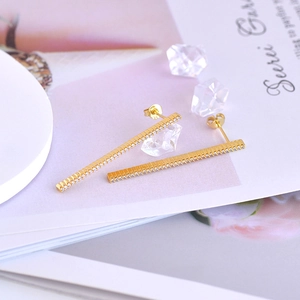 Detailed view of long gold bar earrings with colorful cubic zirconia on a minimalist base