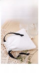 Close-up of a white cotton drawstring pouch with black silk ribbon and custom logo space