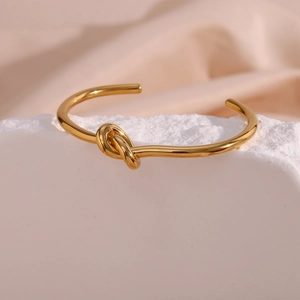 Macro shot of 18K gold plated knotted open bangle on a white stone and pink velvet
