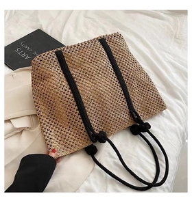 Detailed texture of khaki woven straw tote bag featuring black braided rope handles on bed