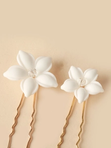 Detail of two white ceramic flower hair pins with crystals and gold U-shaped metal clips