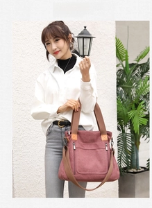 Close-up of a dark pink canvas tote bag with front zippers and brown straps on a model