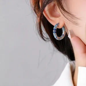 Silver huggie earrings with blue and turquoise crystals shown on a model