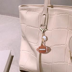 Detail of a rugby pendant and helmet keychain hanging on a white textured handbag