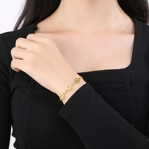 Detail of a golden stainless steel smiley face charm bracelet worn on a model wrist