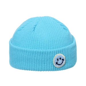 Detail of bright blue ribbed knit beanie featuring a fuzzy smiley face patch applique