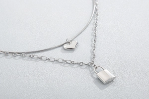 Detailed close-up of double-layer stainless steel necklace with heart and lock pendants