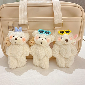 Drie witte pluchen beer-hangers met gekleurde zonnebrillen aan een beige tas