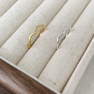 Minimalist gold and silver wavy rings displayed in a luxury cream velvet wooden jewelry box