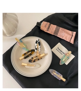 Flat lay of colorful acetate hair clips with marble patterns on white ceramic and silk