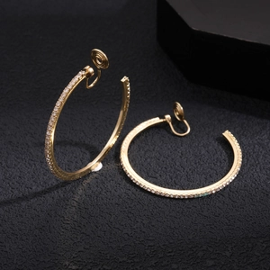 Macro view of gold hoop clip-on earrings with pavé rhinestones on black background