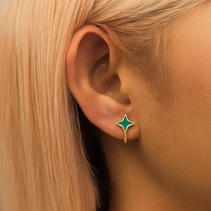 Close-up of a model wearing a gold four-pointed star earring with turquoise enamel finish