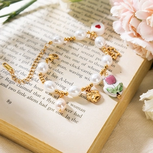 Detail of stainless steel pearl bracelet with tulip and heart charms on a book