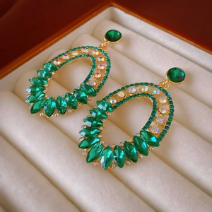 Détail macro de boucles d'oreilles ovales avec de grands strass vert émeraude et blanc cristal