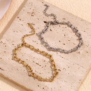Detail of 14K gold and silver U-link anklet chains with lobster clasp on a stone surface