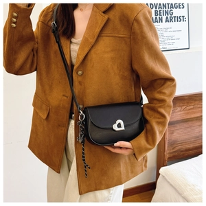 Detail of a black leather saddle bag featuring a silver heart buckle and woven strap decor