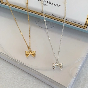 Elegant gold and silver bow pendant necklaces with delicate bead chains in a soft setting