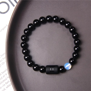 Macro detail of Gemini zodiac bracelet with matte black beads and iridescent charm