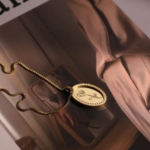 Vintage gold oval rose pendant necklace resting on a magazine in a retro setting