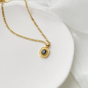 Detail of a vintage gold chain with an oval black gemstone pendant on a white tray