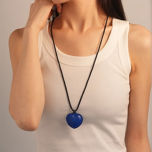 Gros plan d'un pendentif cœur en similicuir bleu sur un collier en corde tressée noire