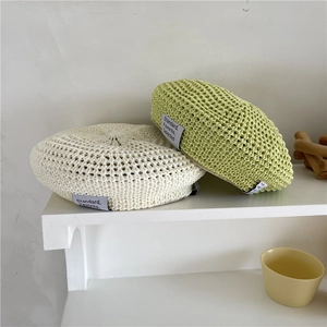Hollow knit straw beret hats in cream and light green displayed on a white shelf