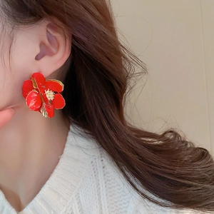 Macro shot of red floral earring with gold edges worn by model in white knitwear