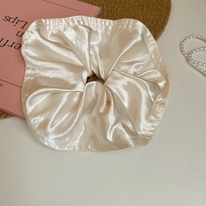 Macro detail of creamy satin scrunchie with soft silk texture on aesthetic background