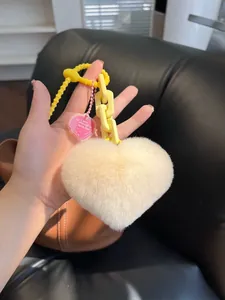 Detail of fluffy beige heart plush keychain with yellow chain and pink heart charm