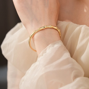 Close-up of a gold bamboo-shaped bangle with inlaid cubic zirconia on a model's wrist