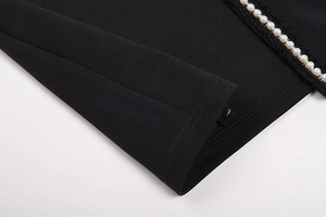 Close-up of black dress fabric featuring white pearl trim with gold metal accents