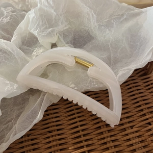 Close-up of semi-circular white translucent resin hair claw clip with metal spring