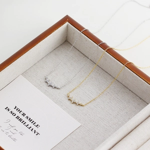 Close-up of gold and silver clover necklaces with clear gems in a wooden jewelry box