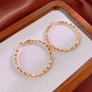Close-up of gold metal hoop earrings featuring geometric diamond-cut faceted texture