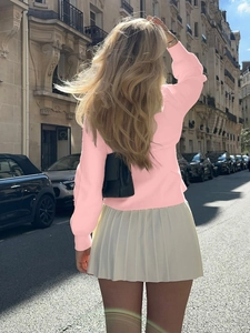 Elegant pink long-sleeve knit sweater paired with a white pleated skirt on city street