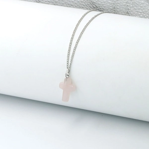 Detail view of a pink stone cross pendant on a silver chain over white cylinder