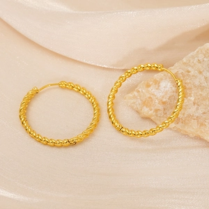 Elegant gold twisted rope hoop earrings displayed on silk fabric with a natural stone accent