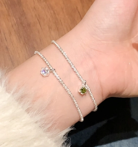 Detailed view of silver stardust bracelets with white and green crystal pendants on wrist