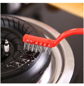 Close-up of red steel wire brush cleaning a gas stove burner with white soapy foam