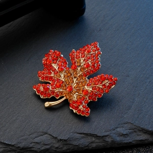 Detailed close-up of a maple leaf brooch with red rhinestones on a dark stone background