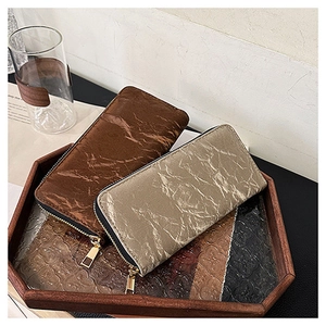 Detailed view of brown and champagne zip wallets with unique crinkled texture on a tray