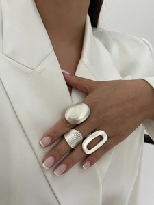 Detailed view of three minimalist silver geometric rings worn with a silk suit