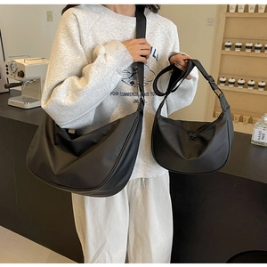 Comparison of large and small black nylon crescent bags worn by a model in a cafe