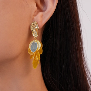 Close-up of geometric gold tassel earrings with yellow shell charms on a female model
